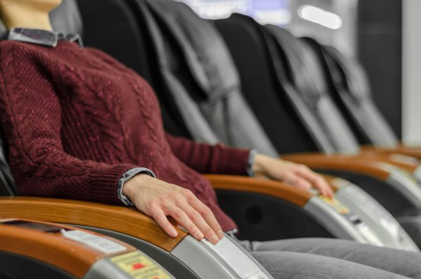 titan ti-7700 massage chair features zero gravity woman in burgundy sweater sits in massage chair getting a massage black massage chairs in a row in the background